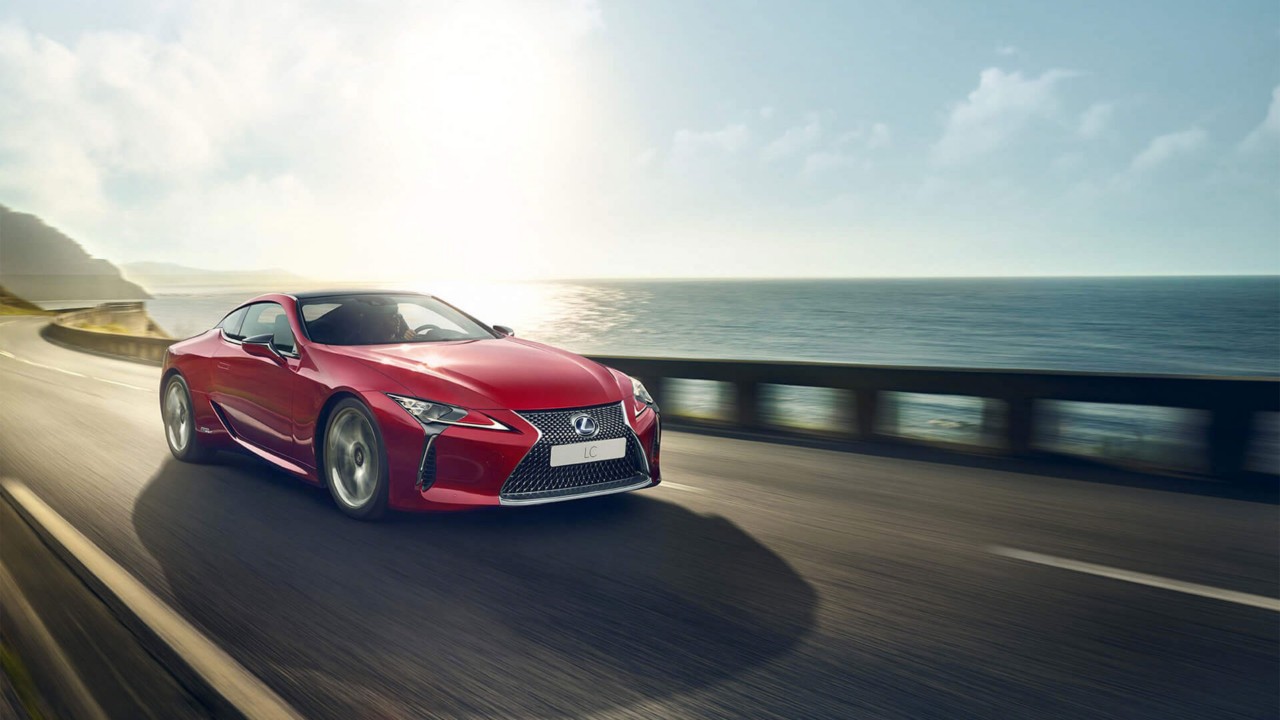 A red Lexus driving next to the water